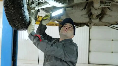 Professional mechanic checking undercarriage with flashlight, working underneath Stock Photos