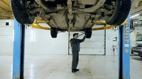 Professional mechanic using a tool while inspecting the undercarriage of a Stock Photos