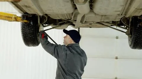 Professional mechanic using tools while inspecting the undercarriage of a lifted Stock Photos