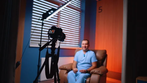 Professional medic in blue uniform talks to camera sitting in an armchair. Stock Footage 334339319