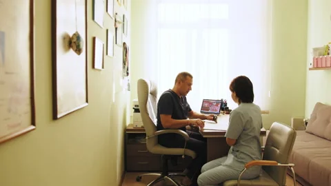 Professional middle aged doctor is talking to his colleagues, while sitting at Stock Footage 174323875
