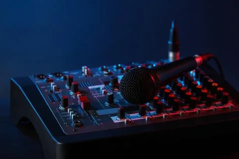 Professional mixing console with microphone on table against dark blue back.. Stock Photos