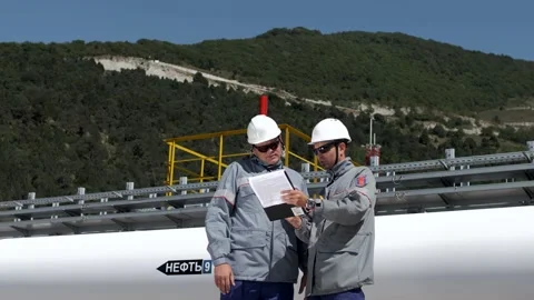 Professional oil workers stand at a large white oil pipeline Stock Footage 130185476