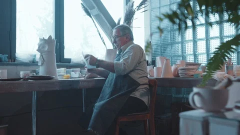 Professional old bearded potter in muddy apron looks at kis art sketch thinking Stock Footage 124850453