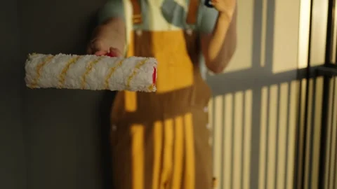 Professional painter comparing pristine and worn paint rollers near sunlit Stock Footage 310903432