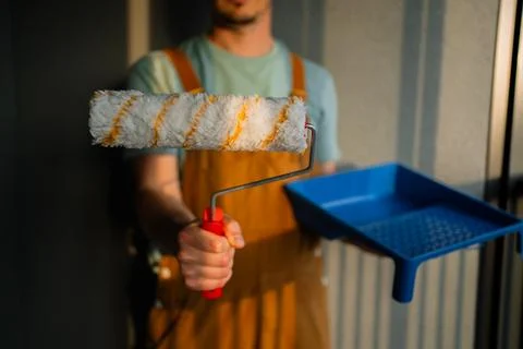 Professional painter gripping paint roller near blue tray, preparing interior Photos