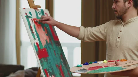 Professional painter guy holds palette painting picture on canvas near easel Stock Footage 175452998