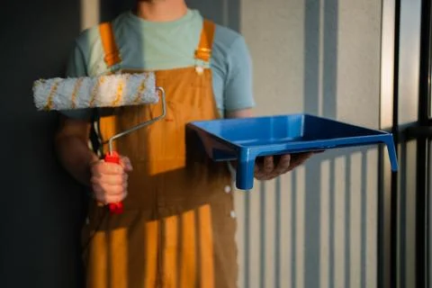 Professional painter holding paint roller, standing near tray, preparing wall Photos