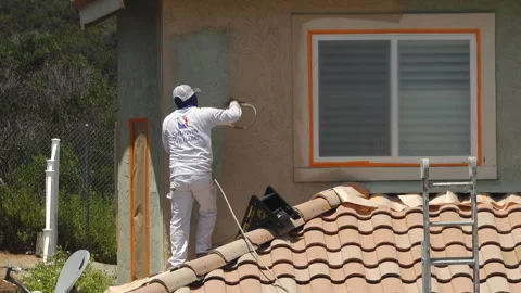Professional painter using a sprayer to paint the stucco on a home Stock Footage 133612823