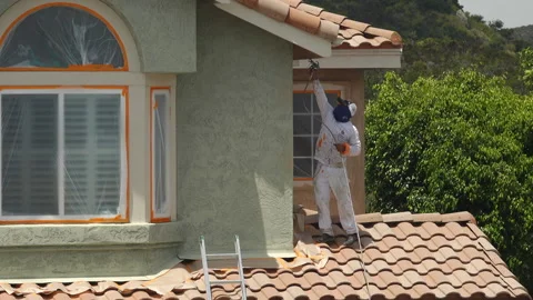 Professional painter using a sprayer to paint the stucco on a home Stock Footage 133612833