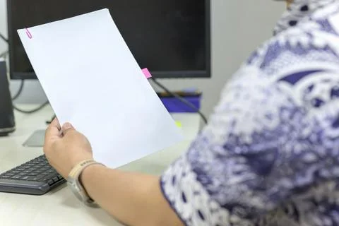A professional in a patterned shirt reviews a stack of white papers with a .. Stock Photos