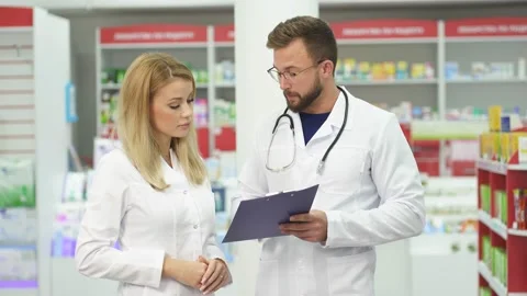 Professional pharmacist having conversation with intern in modern pharmacy Stock Footage 143173380