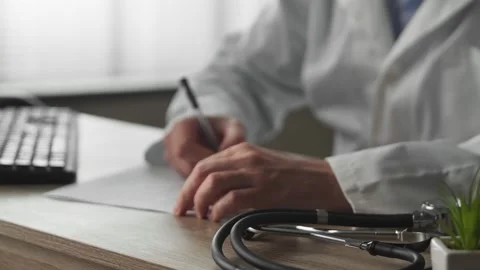 Professional physician gp wearing white coat writing notes using PC at desk Stock Footage 169013058