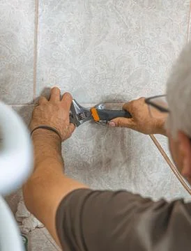 Professional plumber working with an adjustable wrench on pipe fittings duri 库存照片