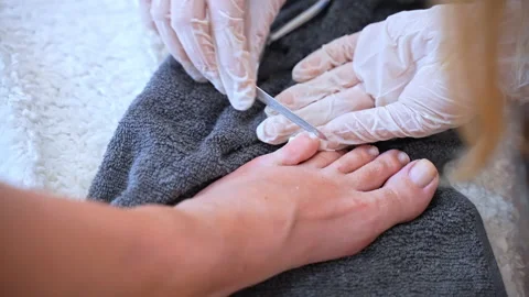 Professional podiatrist in white gloves using hardware file to polish toe nail Stock Footage 234979518