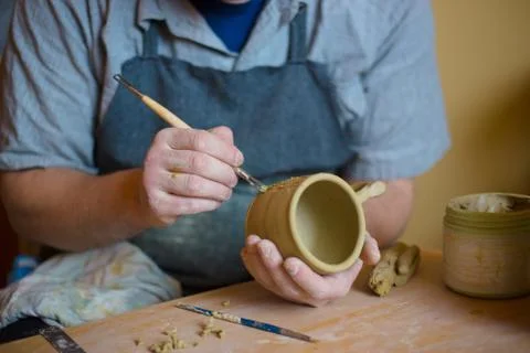 Professional potter making pattern on clay mug with special tool in pottery Stock Photos