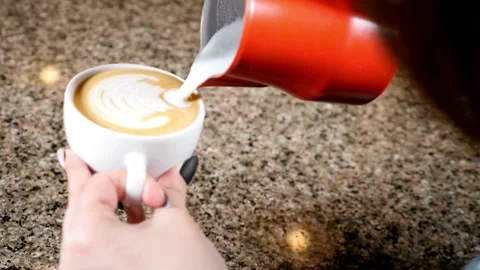 Professional pouring stream milk to create a latte art pattern in white cup. 動画素材 334649988