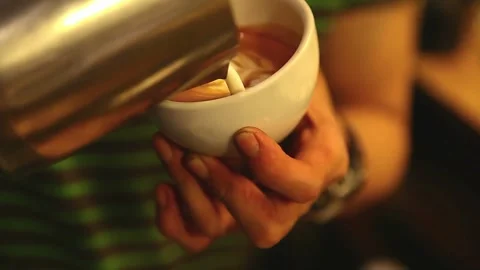 Professional pouring stream milk to create a latte art pattern in white cup. 動画素材 334650175