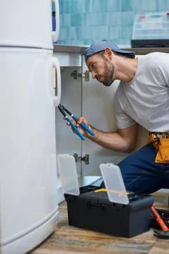 Professional repairman looking focused, using pipe wrench while examining and Stock Photos