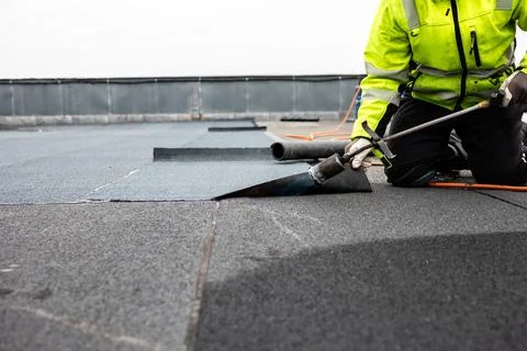 Professional roofer applying bitumen roll on flat roof with a gas burner at.. Stock Photos