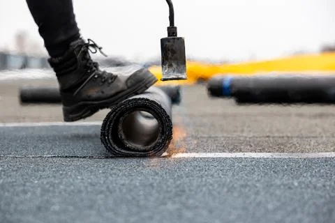 Professional roofer at work securing rolled tar paper with a blowtorch on a.. 스톡 사진