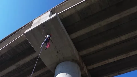 Professional rope access technician inspecting concrete bridge from underneat Stock Footage 306582125
