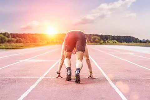 Professional runner taking ready to start position against bright sunlight Stock Photos