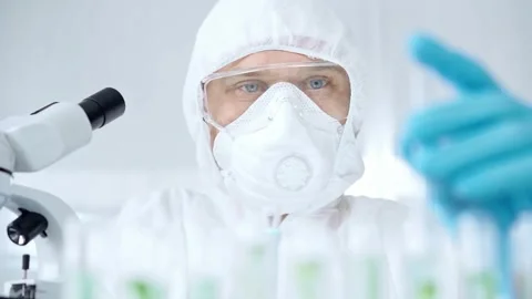 Professional scientist in protective gear is using pipette and examining a test Stock Footage 276671805