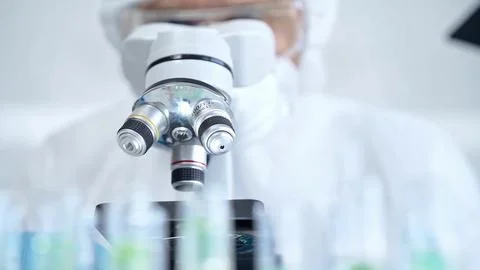 Professional scientist in protective gear is using microscope in a laboratory Stock Photos