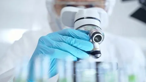 Professional scientist in protective gear is using microscope in a laboratory Stock Photos