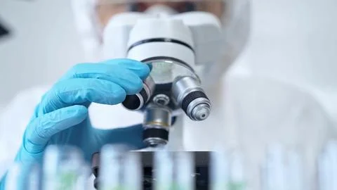 Professional scientist in protective gear is using microscope in a laboratory Stock Photos