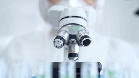 Professional scientist in protective gear is using microscope in a laboratory Stock Photos