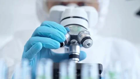 Professional scientist in protective gear is using microscope in a laboratory Stock Photos
