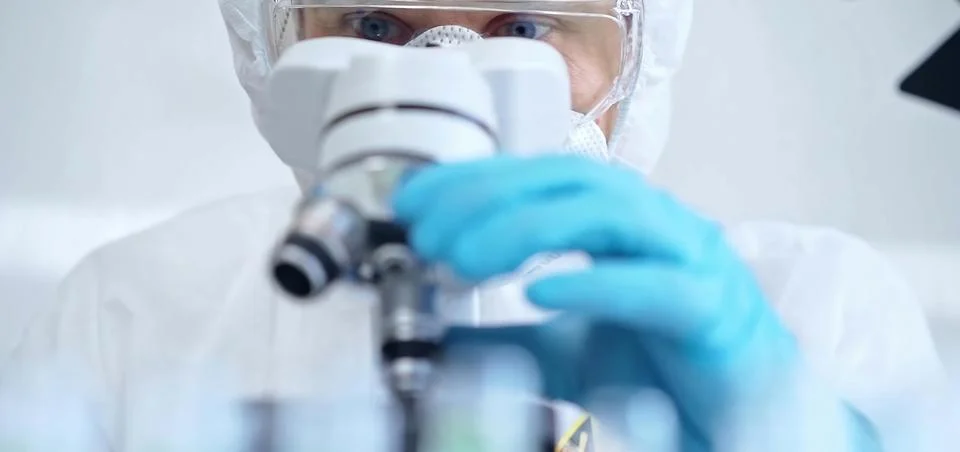 Professional scientist in protective gear is using microscope in a laboratory 스톡 사진
