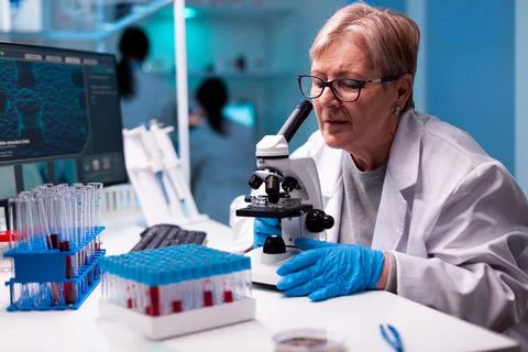 Professional senior scientist using microscope in health study Stockfoto's