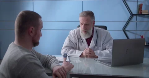Professional serious focused middle aged hoary physician in medical coat sitting Stock Footage 148391588