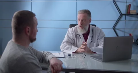 Professional serious focused middle aged hoary physician in medical coat sitting Video stock 148471554