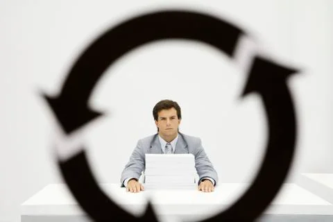 Professional sitting at desk with large stack of paper, circular arrow symbol in Stock-Fotos