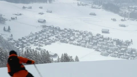 Professional skier freeriding down a mountain with village in background Stock Footage 129084668