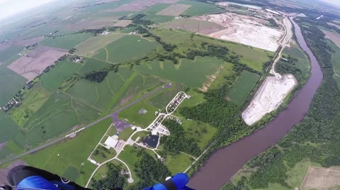 Professional skydiver parachuting in blue sky above green flatland and river Stock Footage 67237199
