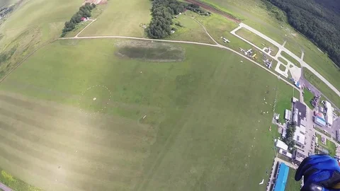 Professional skydiver parachuting down to green field in sunny day. Landscape Stock Footage 70533024