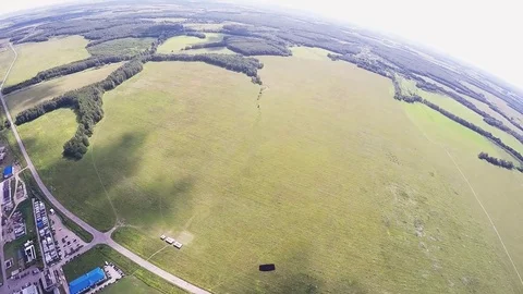 Professional skydiver parachuting, fly over green field in sunny day among other Видео 70532635