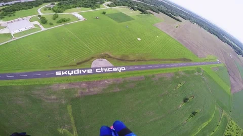 Professional skydiver parachuting in grey sky above green flatland. River Stock Footage 67237461