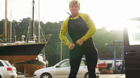 Professional surfer adjusting his wetsuit outside in harbour on sunny day Stock Footage 163333384