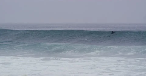Professional surfer paddling over ocean waves during cloudy day in Nazare Stock Footage 156016155