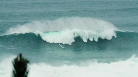 Professional surfer riding down huge ocean wave with jet ski drivers around Stock Footage 163266871