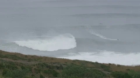 Professional surfer riding tall waves in stormy ocean on overcast day in Nazare Video stock 157700486