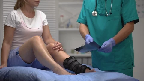 Professional surgeon talking about broken bone x-ray to female in ankle wrap Stock-Footage 117176487