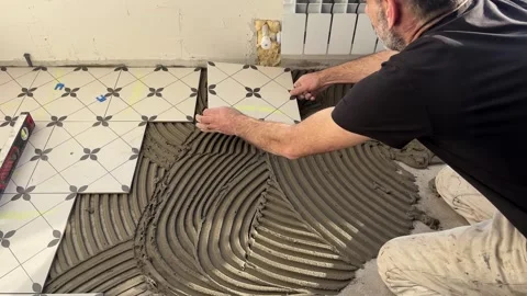 Professional tile installer spreading tile adhesive with a notched trowel on the Stock Footage 346690806
