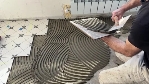 Professional tile installer spreading tile adhesive with a notched trowel on the Stock Footage 346811226